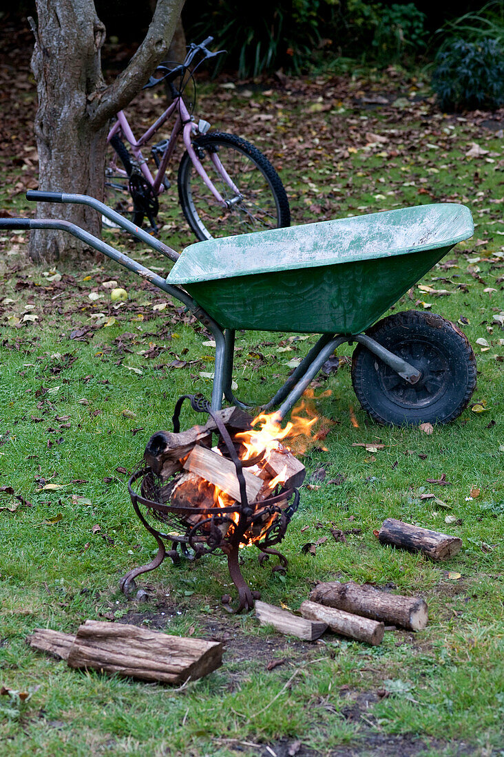 Schubkarre und Fahrrad mit brennenden Holzscheiten in einem schmiedeeisernen Gartenofen, Yeovil, Somerset, England, UK
