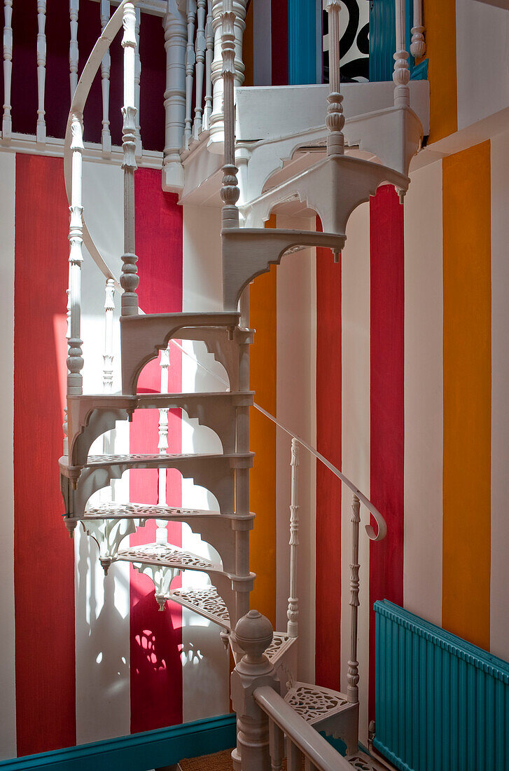Schmiedeeiserne, weiß lackierte Wendeltreppe mit bunt gestreifter Tapete in einem Haus in Großbritannien