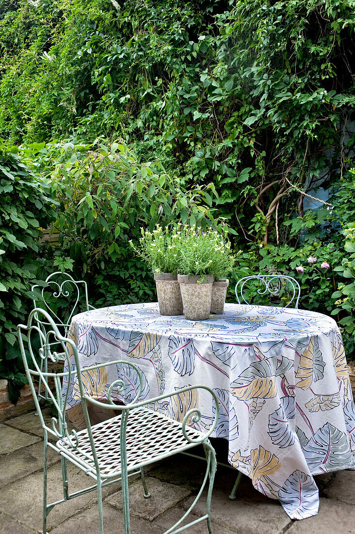 Schmiedeeiserne Stühle am Tisch mit Blattmotivtuch im Garten eines Londoner Hauses UK
