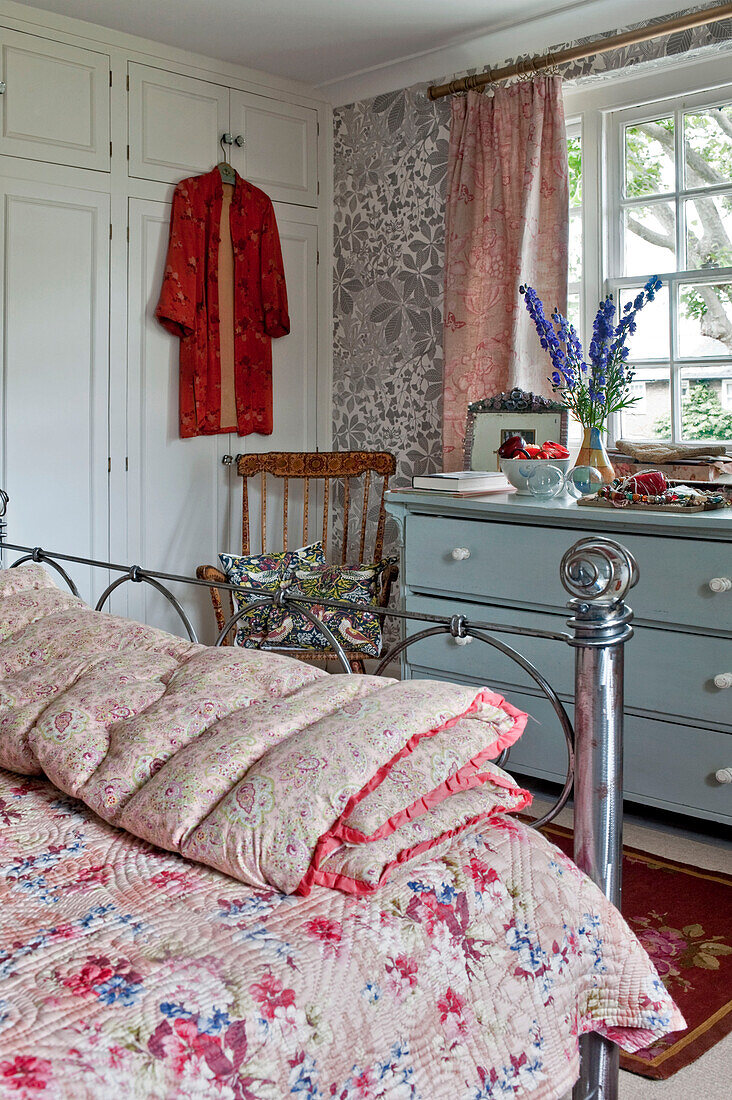 Painted chest of drawers and quilts on metal framed bed in London home UK
