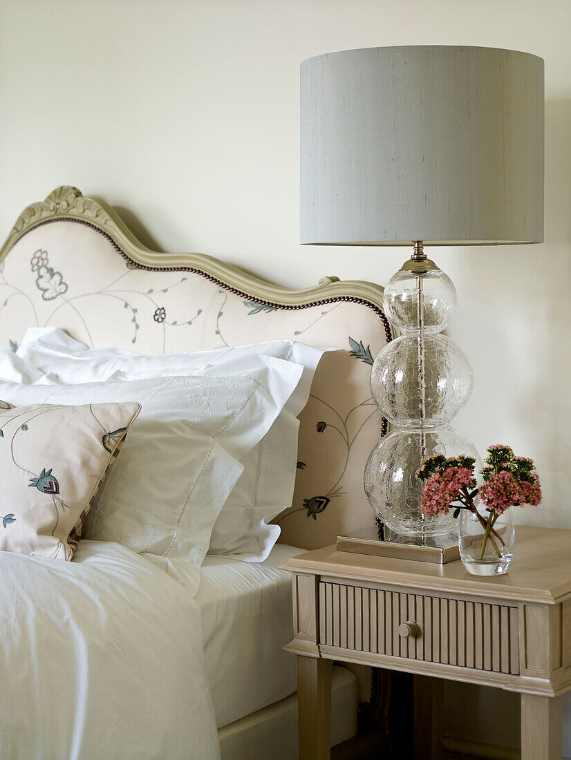 Co-ordinating headboard and pillow with glass lamp on bedside table in West London townhouse England UK