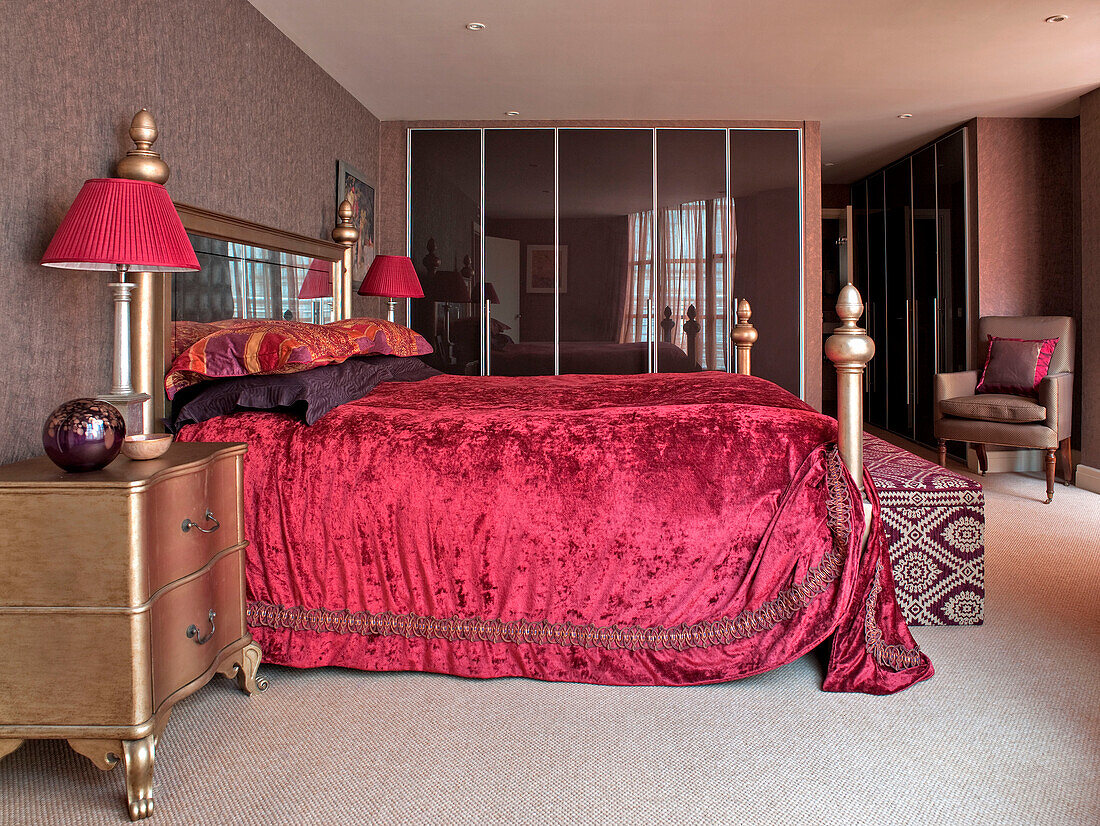 Red velvet bed cover and metallic side unit in bedroom of London apartment England UK
