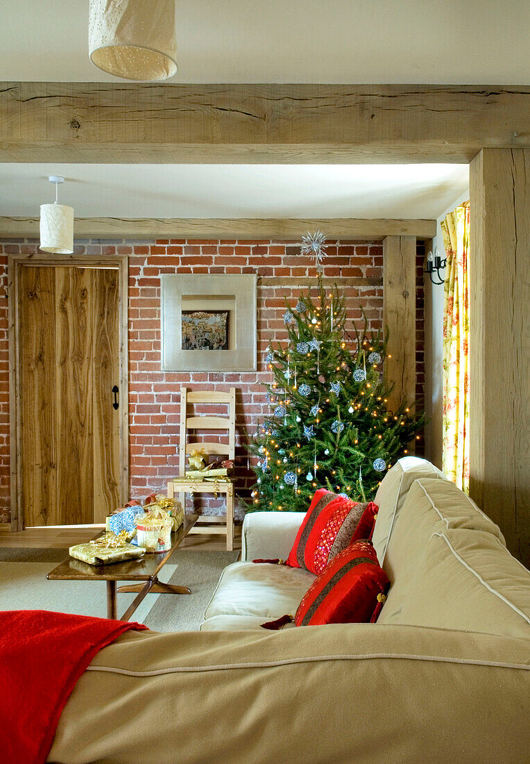 Christmas tree set against exposed brick wall in timber framed rural Suffolk home England UK