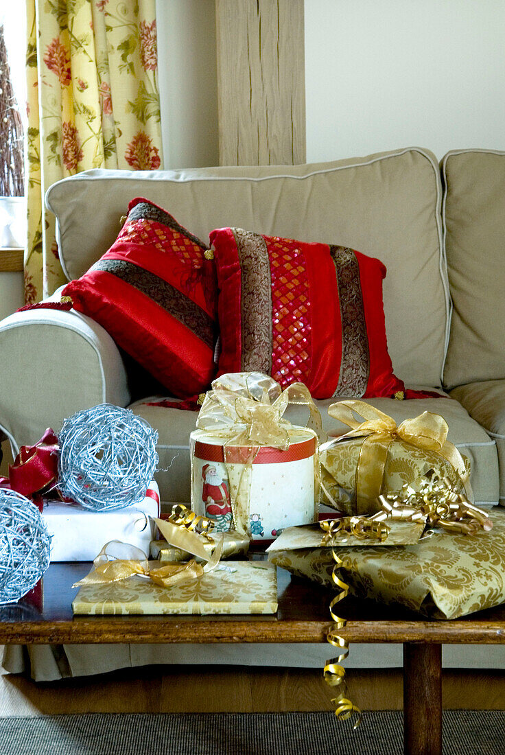 Eingepackte Geschenke auf dem Tisch vor dem Sofa mit roten Kissen im Wohnzimmer eines Hauses im ländlichen Suffolk England UK