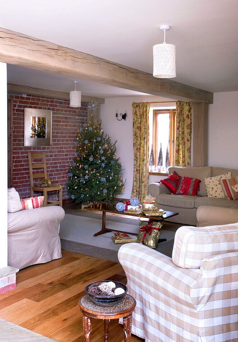Weihnachtsbaum an einer freiliegenden Ziegelwand im Wohnzimmer eines Hauses im ländlichen Suffolk, England, UK