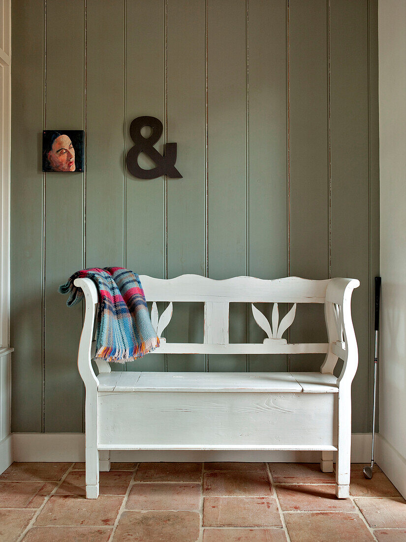 Ampersand on panelled wall with artwork above salvaged garden bench painted white in Suffolk family home England UK
