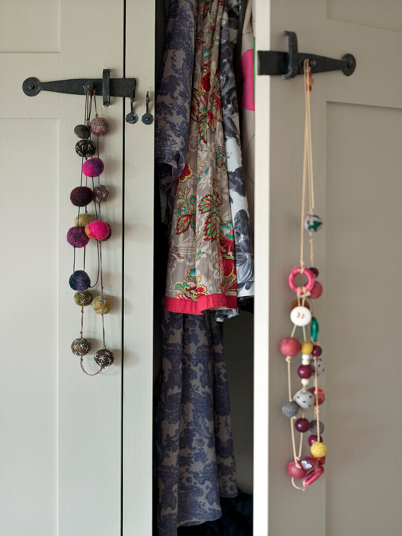 Beaded jewellery hangs on doorlatch of open wardrobe with floral clothes in Suffolk family home England UK