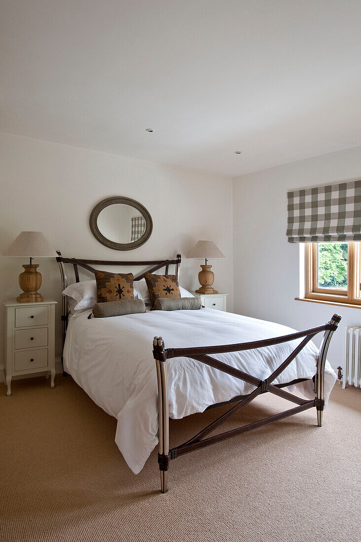 Unique leather strapped footboard on bed with checked blind and matching lamps in Canterbury home England UK