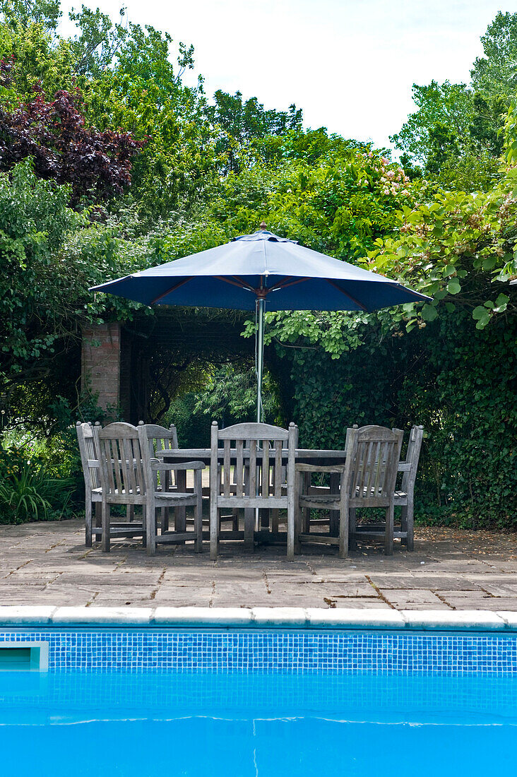 Tisch und Stühle am Pool mit Sonnenschirm auf dem Grundstück eines Hauses in Canterbury, England UK