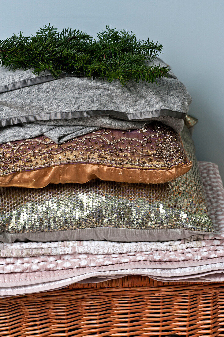 Folded quilt and cushions with sprig of pine on basket in Forest Row family home, Sussex, England, UK