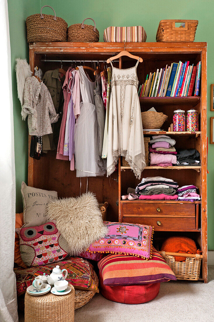 Kleider, Bodenkissen und Garderobe im Mädchenzimmer eines Familienhauses in Forest Row, Sussex, England, UK