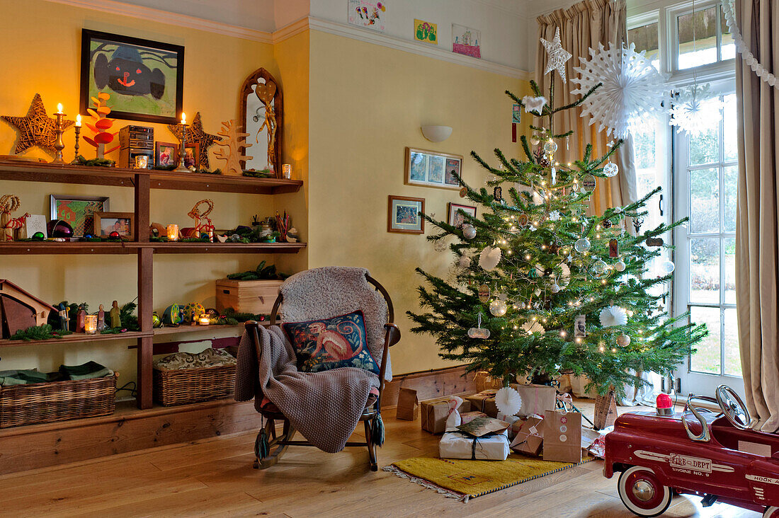 Weihnachtsbaum und Schaukelstuhl mit Regalen in einem Familienhaus in Forest Row, Sussex, England, UK