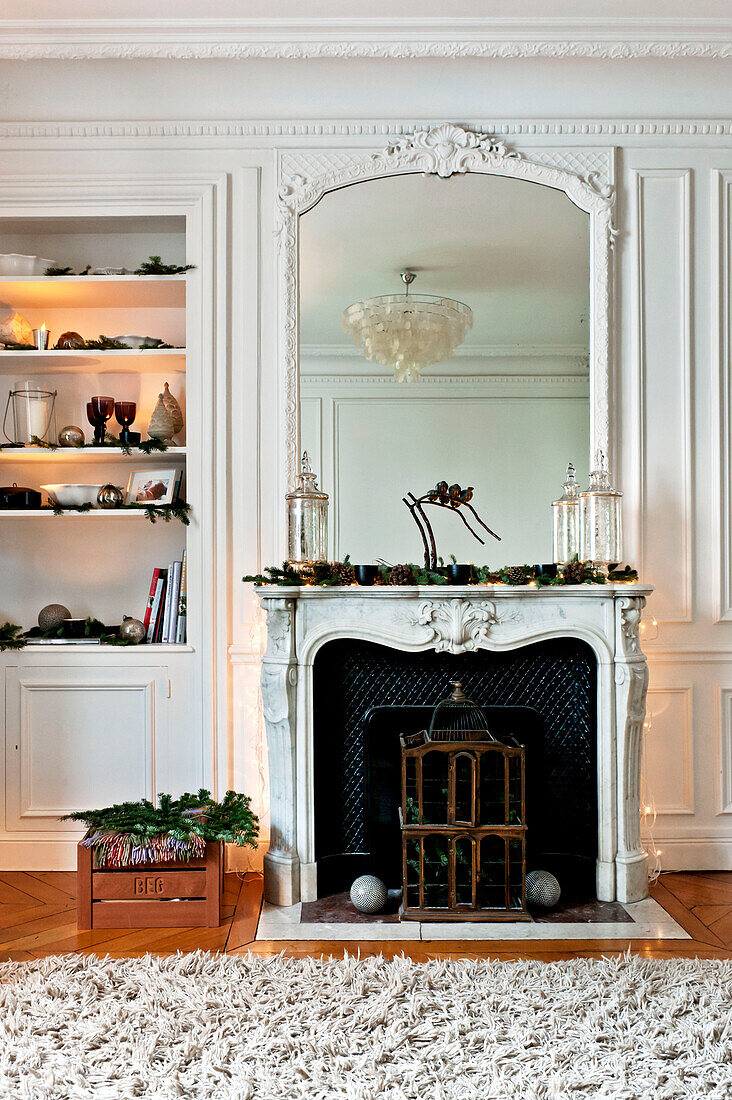 Mirror on marble fireplace with birdcage and recessed shelving at Christmas, in Paris apartment, France