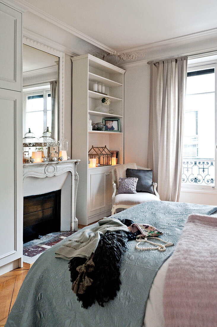Clothes and blankets on bed in room with mirror and shelving unit in Paris apartment, France