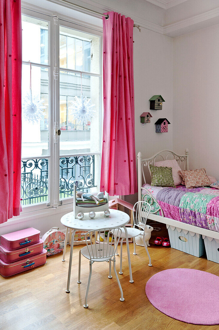 Tisch und Stühle vor einem Fenster mit Vorhängen in einem Mädchenzimmer in einer Pariser Wohnung, Frankreich