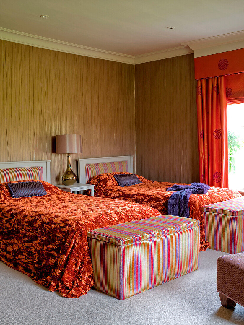 Orange bed covers in twin room with upholstered blanket boxes in rural Suffolk home England UK