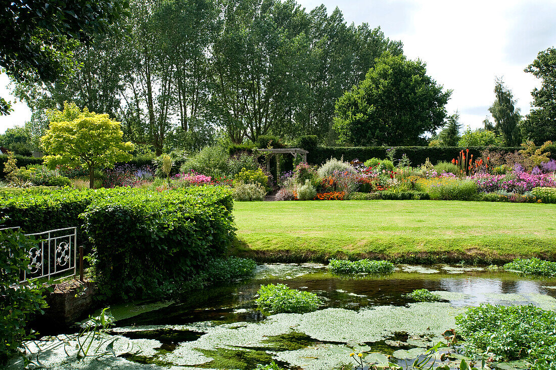 Footbridge over pond in rural garden of Suffolk country house England UK