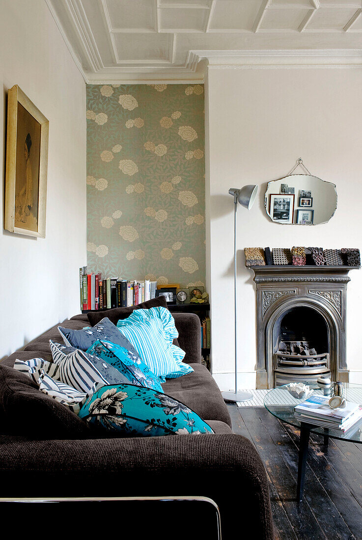 Turquoise patterned cushions on sofa with vintage fireplace in London home, UK