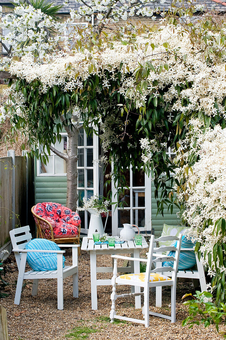 Bemalter Tisch und Stühle unter blühenden Blüten im Garten eines Londoner Hauses, UK