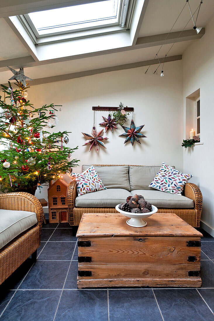 Korbsofa und hölzerner Couchtisch mit Weihnachtsbaum im Wintergartenanbau eines Hauses in Walberton, West Sussex, England, UK