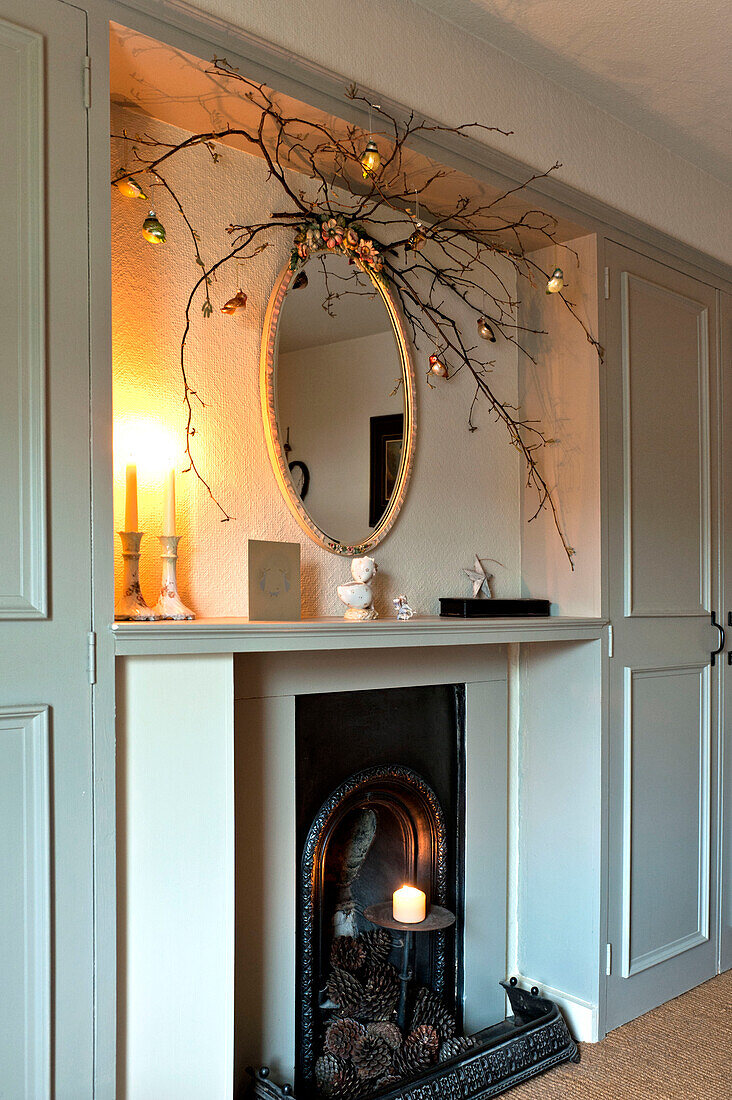 Twig arrangement and oval mirror with lit candles at fireplace in Walberton home, West Sussex, England, UK