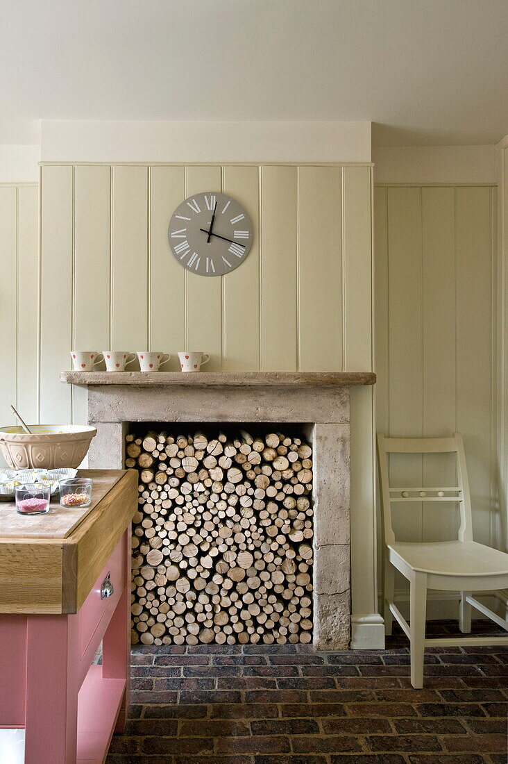 Chair beside fireplace full of logs in kitchen of Buckinghamshire home, England, UK
