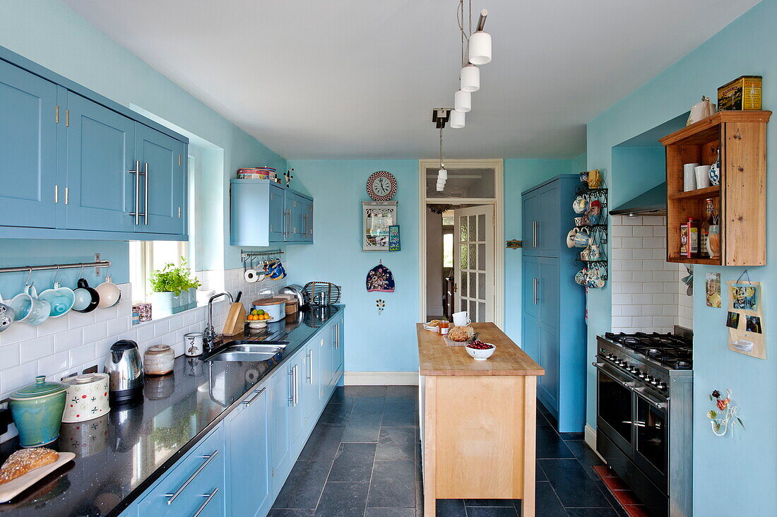 Kochinsel aus Holz in blauer Einbauküche eines Familienhauses in Bovey Tracey, Devon, England, UK