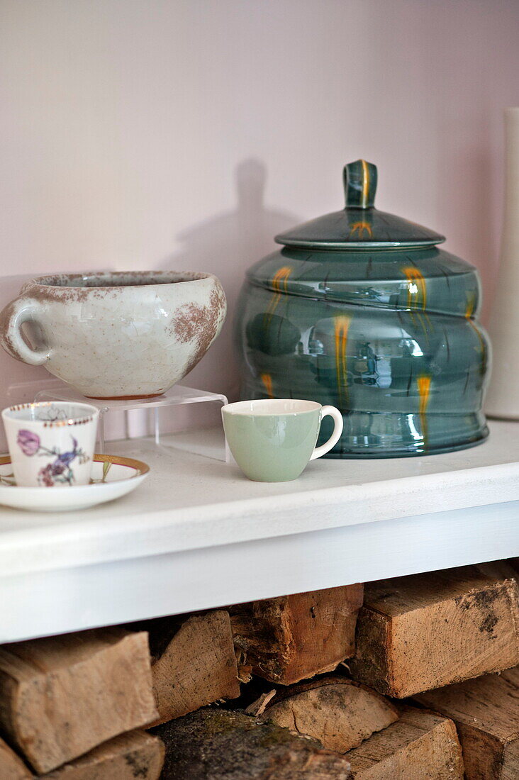 Handbemalte Keramik mit Brennholz auf einem Regal im Haus der Familie Bovey Tracey, Devon, England, UK