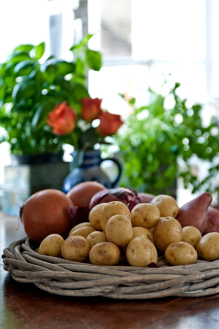 Zwiebeln und Kartoffeln in einem geflochtenen Korb in der Küche eines Bauernhauses in Suffolk, England, UK