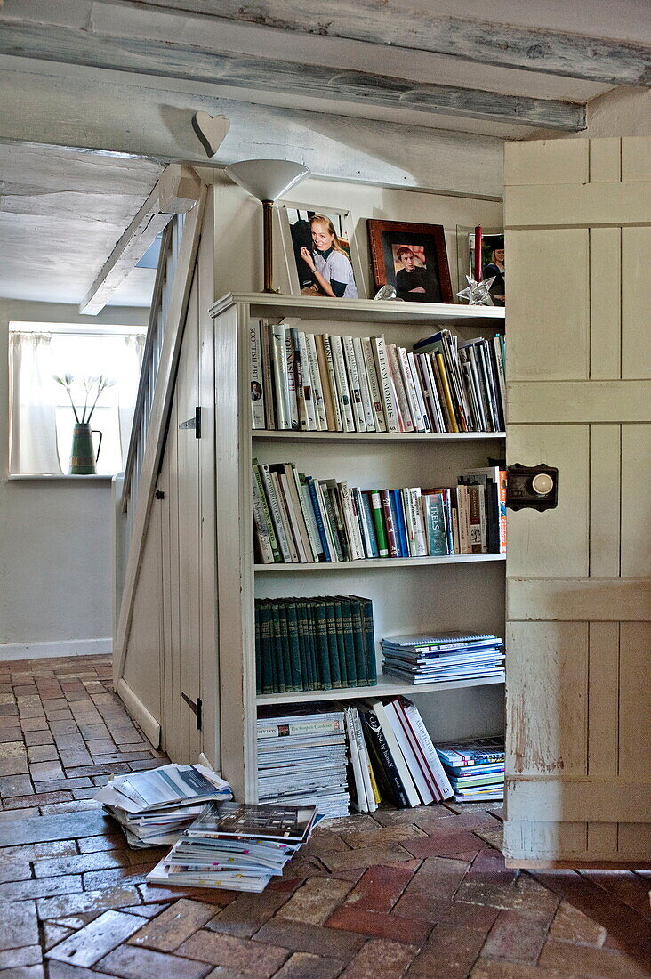 Bücherregal und Zeitschriften in gemauerter Eingangshalle eines Bauernhauses in Suffolk, England, Vereinigtes Königreich