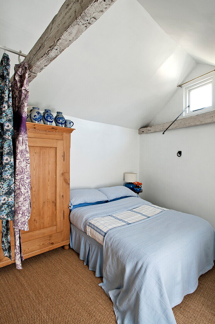 Doppelbett mit hölzernem Kleiderschrank und Kleidern im Dachgeschoss eines Bauernhauses in Suffolk, England, UK