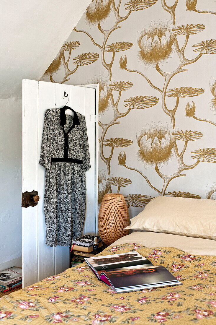 Damenkleid hängt an der Rückseite der Tür im Schlafzimmer mit großformatiger Tapete in einem Bauernhaus in Suffolk, England, UK