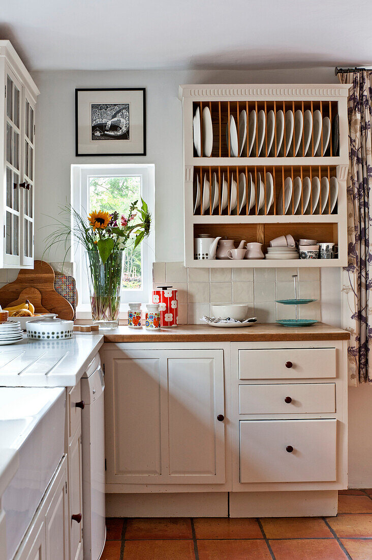 Cut flowers and plate rack in white fitted kitchen of Hertfordshire home, England, UK