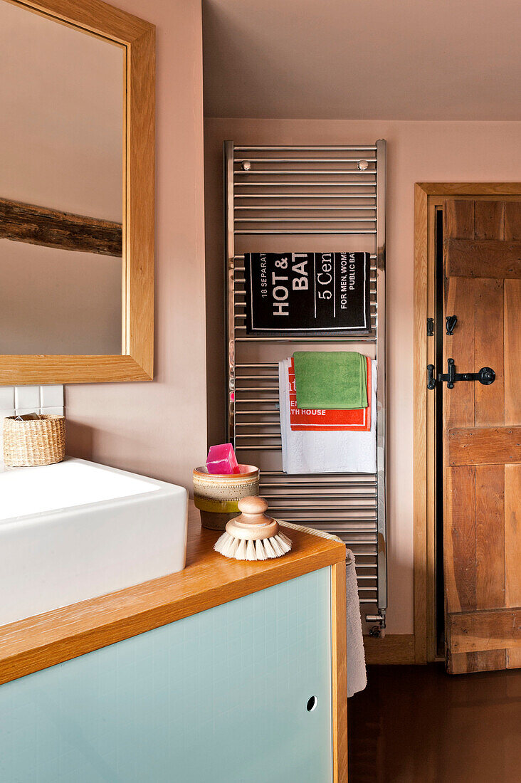 Badematten und Handtücher hängen an einem beheizten Regal in einem pastellrosa Badezimmer in Hertfordshire, England, UK