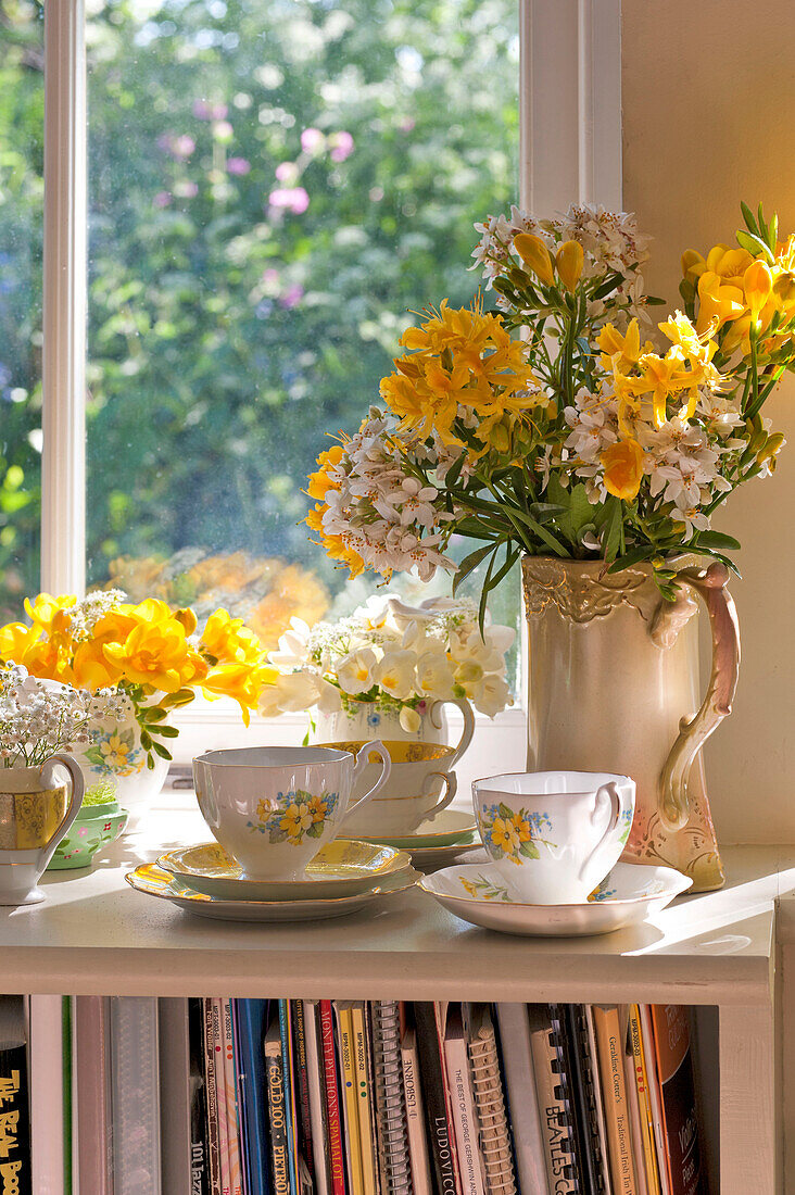 Teetassen und Schnittblumen auf der sonnenbeschienenen Fensterbank eines Hauses in Essex, England, Vereinigtes Königreich