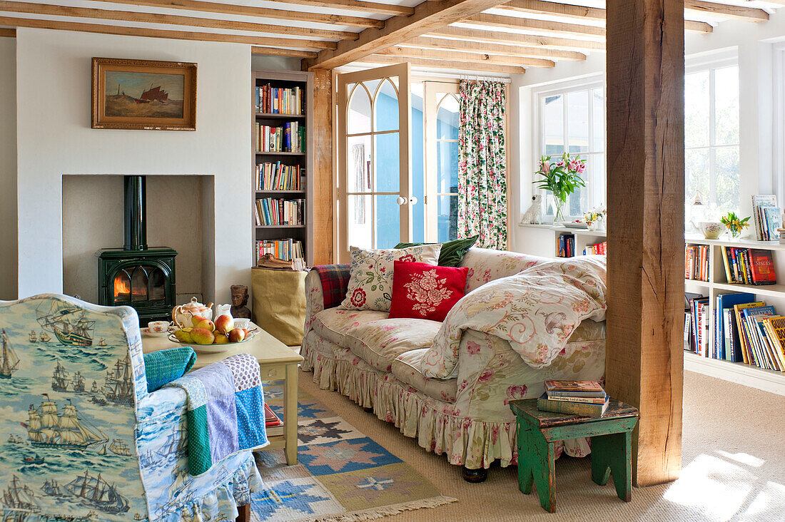 Bücherregale in einem Wohnzimmer mit Balken und Holzofen, der die Sitzecke in einem Haus in Essex, England, UK, beheizt