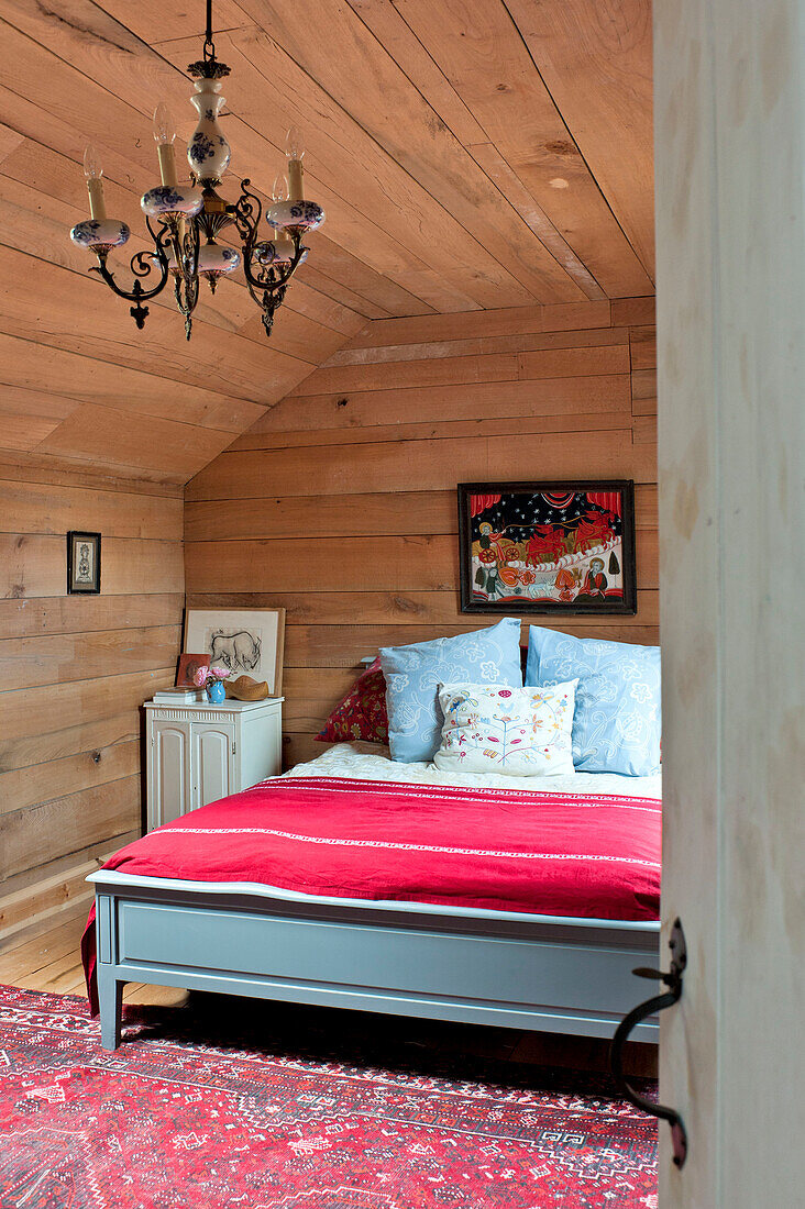 Doppelbett mit roter Decke in einem holzverkleideten Raum mit Vintage-Leuchten, Haus in Essex, England, UK