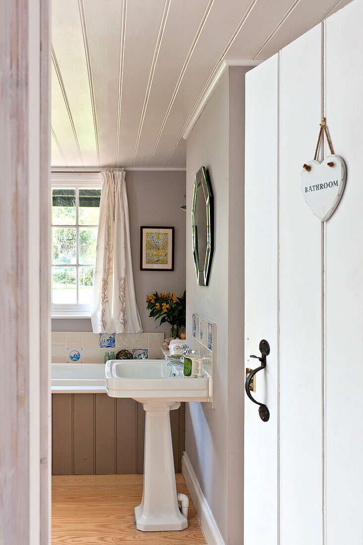 View through panelled door to pedestal basin in white bathroom of Essex home, England, UK