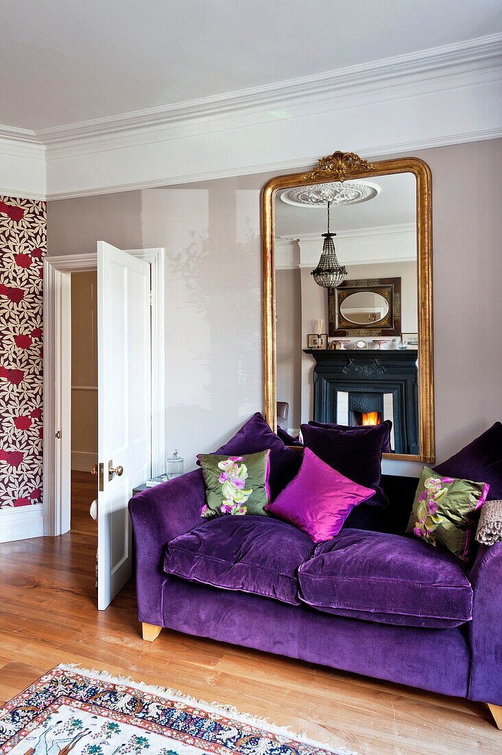 Lila Zweisitzer-Sofa mit vergoldetem Spiegel, der den Kamin im Haus einer Familie aus Middlesex reflektiert, London, England, UK