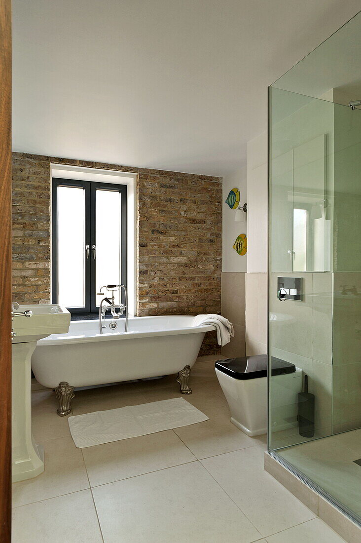 Freistehende Badewanne mit freiliegender Wand und Duschkabine im Badezimmer eines Hauses in London, England, UK