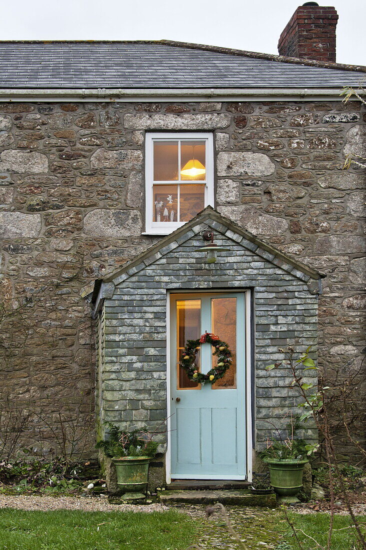 Weihnachtsgirlande an der Verandatür eines Bauernhauses aus Stein in Cornwall, England, Vereinigtes Königreich