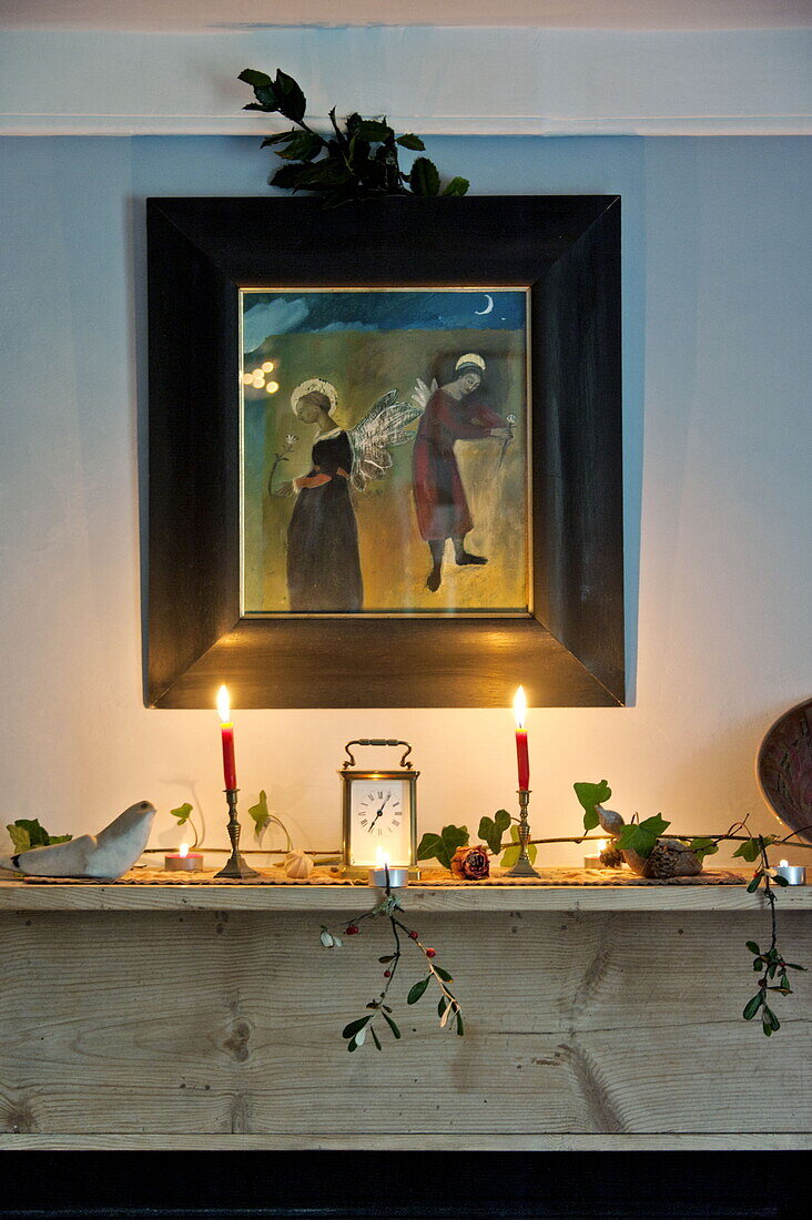 Artwork with lit candles above wooden mantlepiece in farmhouse, Cornwall, England, UK