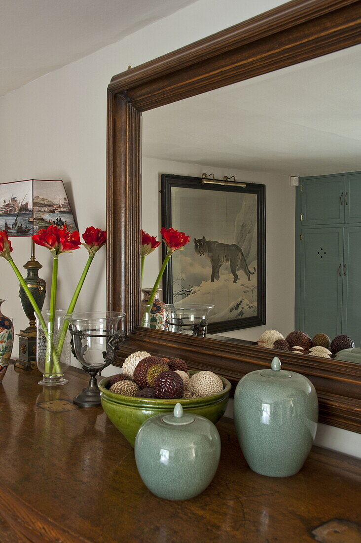 Cut flowers and ornaments on sideboard with wooden framed mirror in contemporary Suffolk country house, England, UK