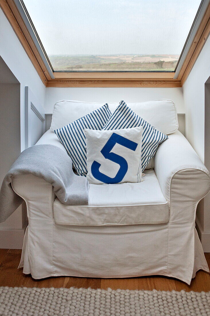White slip cover on armchair at window of attic bedroom in Wadebridge home, Cornwall, England, UK