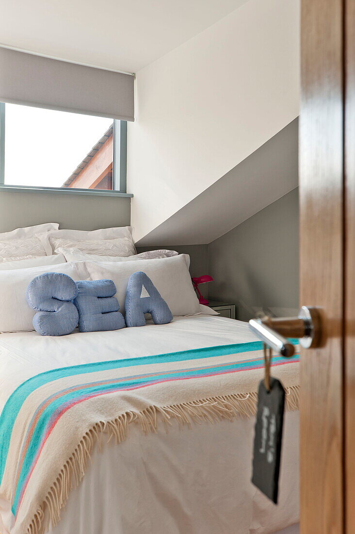 Gestreifte Decke und Kissen mit dem Schriftzug 'SEA' auf dem Doppelbett unter dem Fenster in einem Haus in Wadebridge, Cornwall, England, UK