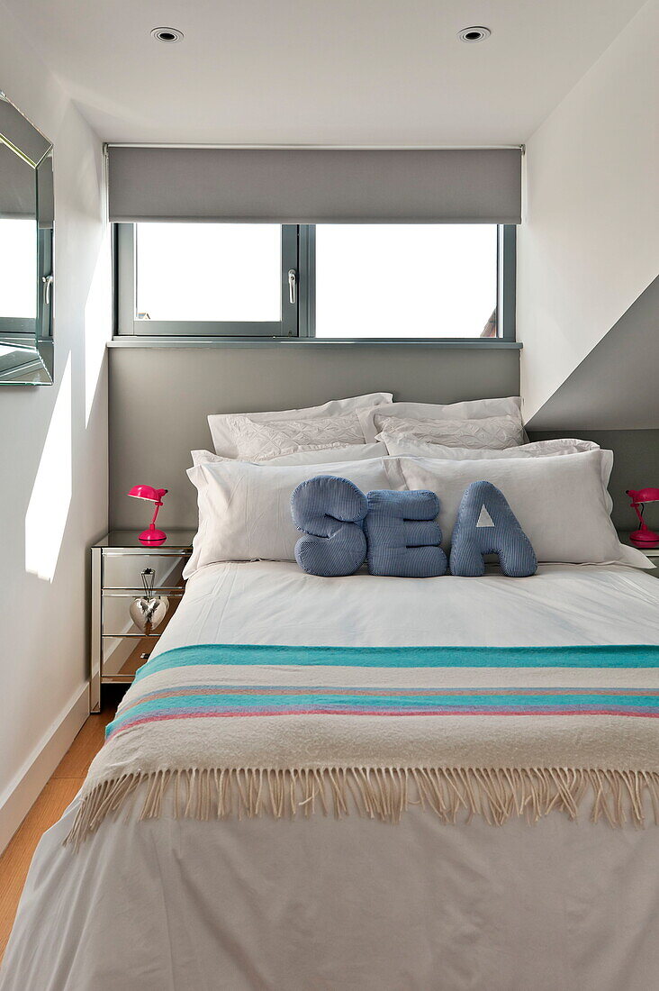 Striped blanket and cushions with the word 'SEA' on the double bed under the window in a house in Wadebridge, Cornwall, England, UK