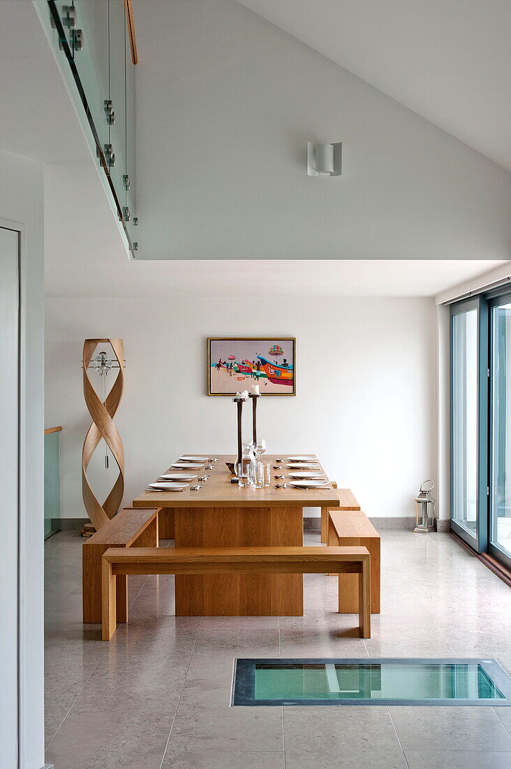 Holztisch und Sitzbänke im doppelhohen Esszimmer eines modernen Hauses, Cornwall, England, UK