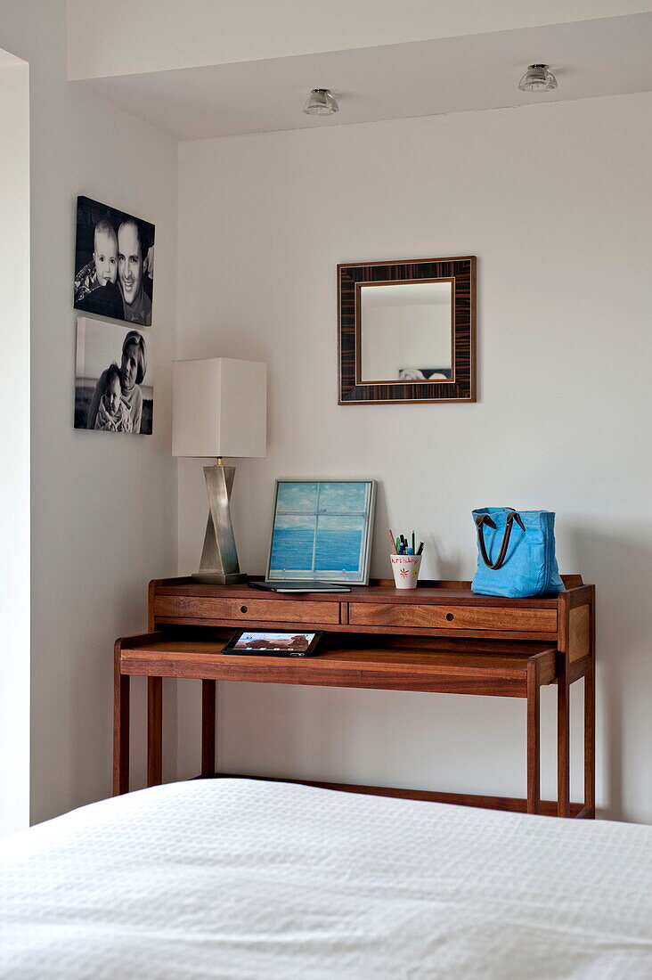Fotografien und Spiegel über einem Holztisch im Schlafzimmer eines modernen Hauses, Cornwall, England, UK