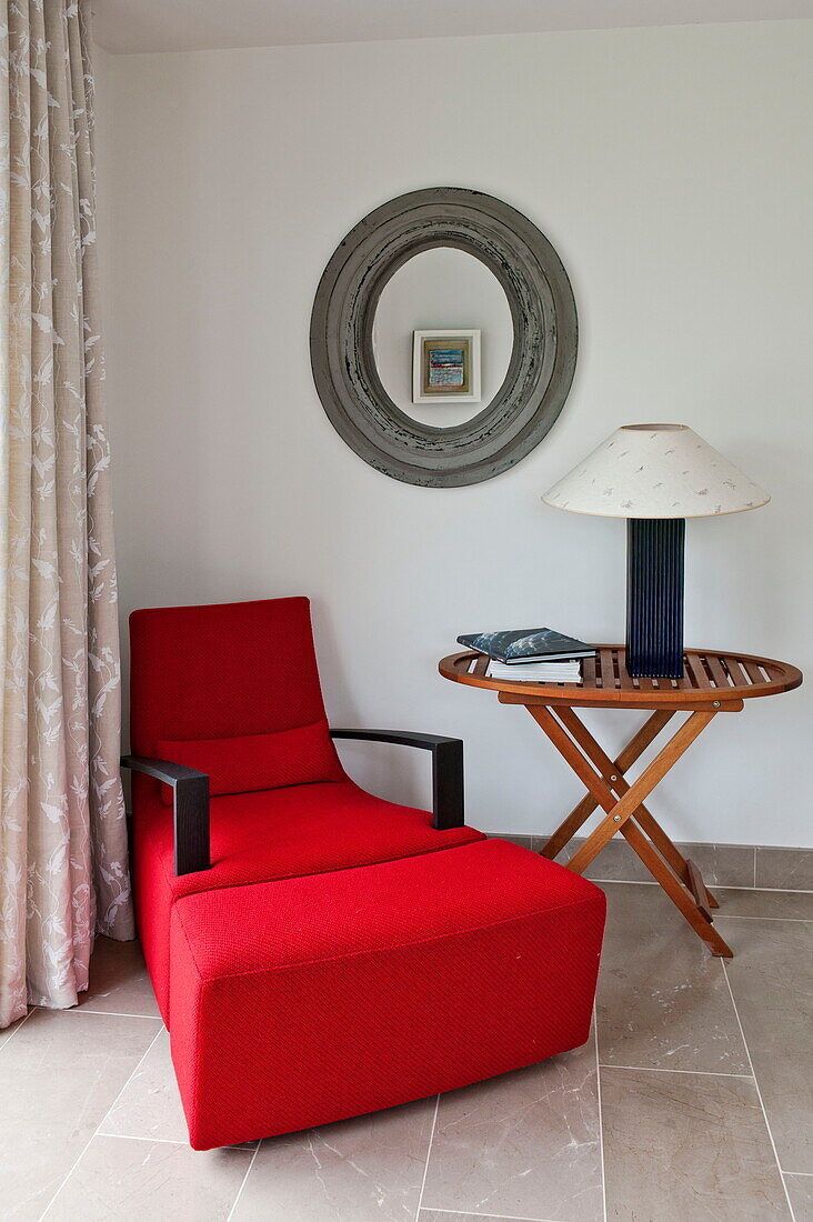 Roter Sessel mit rundem Spiegel und Beistelltisch in einer Ecke eines modernen Hauses, Cornwall, England, UK