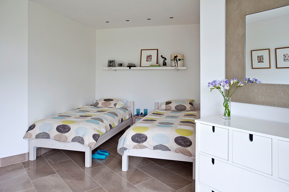 Twin beds with large spots on duvets and white painted storage drawers in contemporary home, Cornwall, England, UK